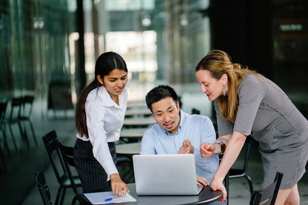 来自不同团队的3人正在一个开放的区域里围绕一台笔记本电脑进行讨论.