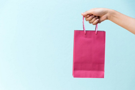 商业妇女手在蓝色具体背景举行粉红色购物袋