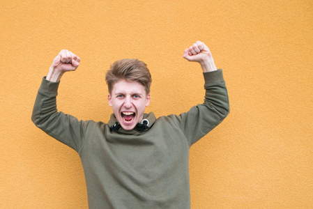 情绪化的学生在橙色墙的背景下从幸福中举起双手照片