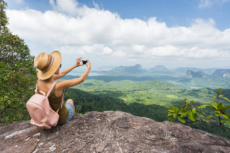 游客从山顶上拍下她的智能手机。Woamn 戴着帽子, 背包坐在岩石上。旅游理念