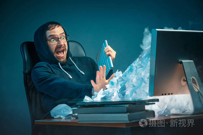 年轻强调英俊的商人工作在办公桌上在现代办公室喊着笔记本电脑屏幕和愤怒的垃圾邮件