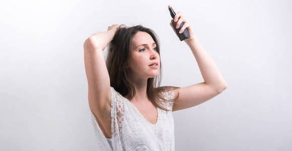 长喷天然化妆品: 一个长头发的女孩喷头发.白色背景上的模型照片