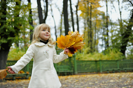 可爱的小女孩在秋天公园举行串黄色树叶