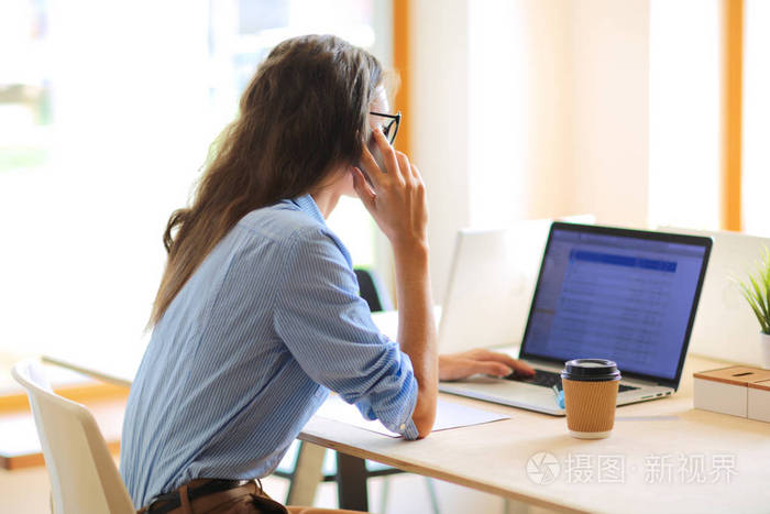 美丽的年轻业务谈的女人坐在办公室桌前在手机上女商人