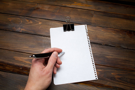 一个人的手中握有笔在白纸上木制的背景。顶视图与副本空间