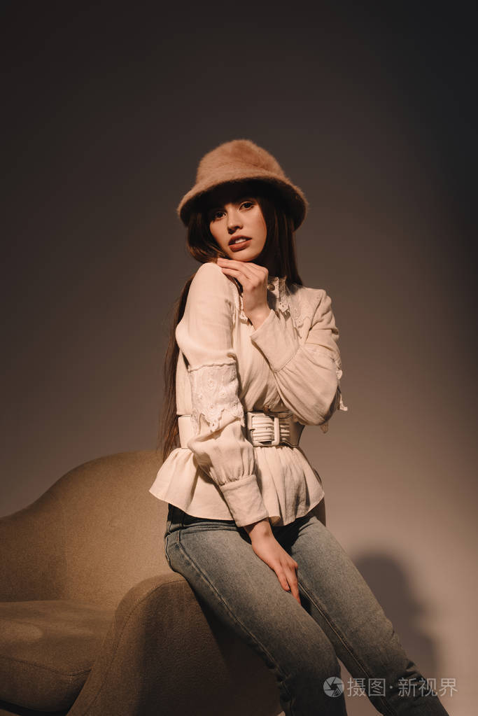 在黑暗背景下坐在扶手椅上的美丽时尚女人的肖像