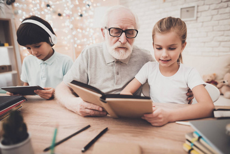爷爷帮助男孩做家庭作业, 而女孩使用平板电脑