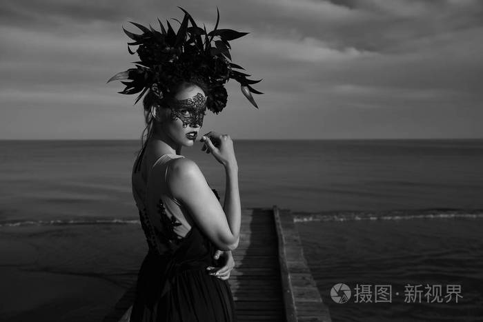 黑色和白色戏剧性的肖像美丽的情绪女人与黑色花边面具脸上和大花冠上的头上的木码头上的立场 背景下的乌云和大海照片 正版商用图片0o3b74 摄图新视界