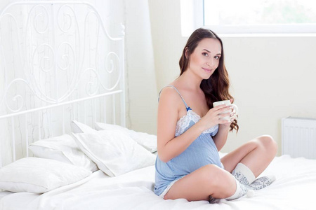 一个年轻的怀孕女人正坐在卧室里。孕妇放松