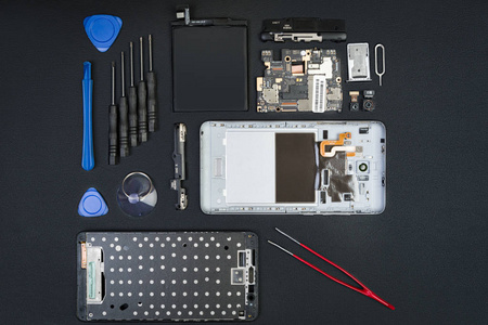 拆卸的智能手机与被删除的屏幕和特殊用途工具在黑色桌面上。flatlay 风格的手机详细信息