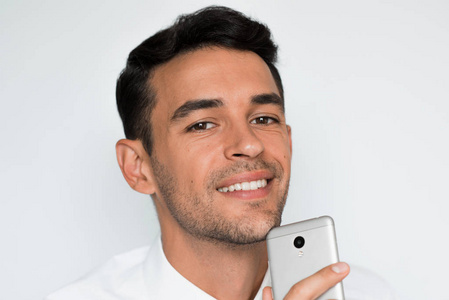 英俊男人的肖像发送手机上的文本与灰色背景隔离。技术和连接理念。年轻的白种商人在演播室用智能手机摆姿势