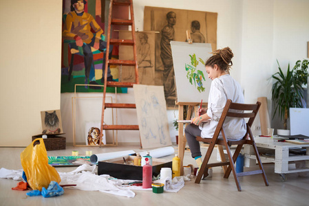 艺术女孩坐在演播室和绘画在画架上