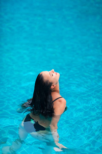 年轻的黑发妇女日光浴游泳池