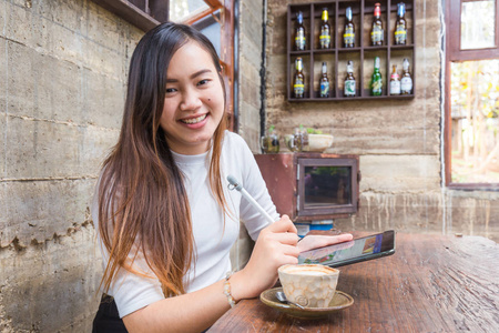 美丽的商业女性使用智能手机和平板咖啡杯在艺术咖啡馆