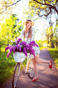 美丽的年轻女孩与老式自行车和花卉在城市背景在阳光下的户外