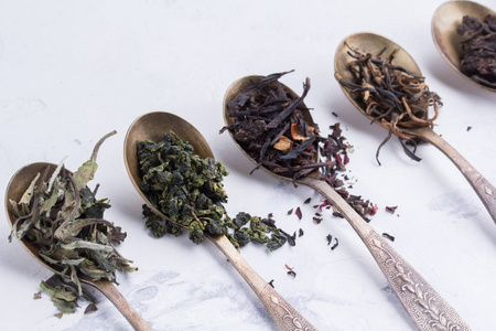 不同种类的茶在古色古香的勺子在白色背景上的干树叶
