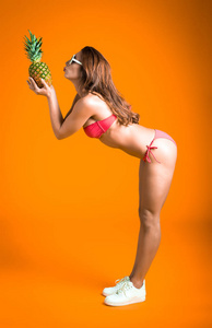 年轻健康美丽的女人的红色比基尼和白色太阳镜新鲜菠萝在手里的画像