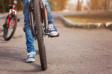 在阳光明媚的春天, 在沥青路上骑自行车的孩子。踏板和脚特写