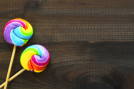 两个彩虹色棒棒糖在蓝色木背景照片
