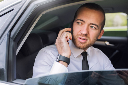 水平特写肖像一个英俊的白种人着急的商人, 电话看着车窗, 坐在汽车后座上。技术和商业理念