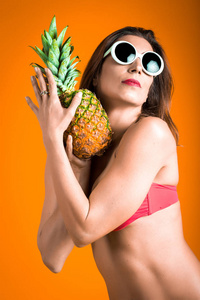 年轻健康美丽的女人的红色比基尼和白色太阳镜新鲜菠萝在手里的画像