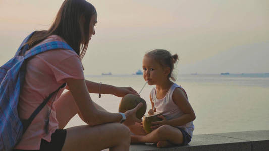 旅行者的母亲和女儿坐在海滨和饮料 coconats
