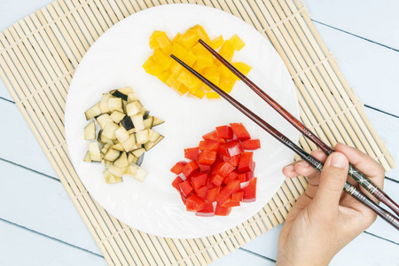 在竹垫子上切碎的蔬菜。手持筷子的女孩的手。木桌上的顶部视图