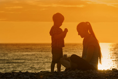 妈妈和儿子在海滩上，石头玩。日落的时候剪影