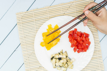 在白色盘子上切下的甜椒和茄子。手中的女性持有食品棒。东厨理念。复制空间