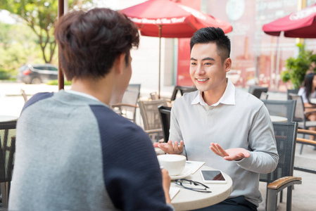 两个年轻英俊商人穿着休闲服微笑着，在咖啡厅聊天