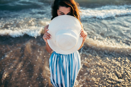 可爱和美丽的女人躲在海背上的白帽子
