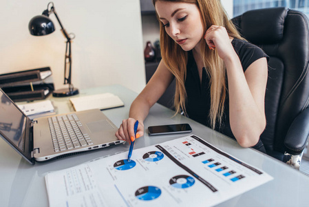 女实业家 readind 财务报告分析的统计数字指向在她的办公桌工作的饼图