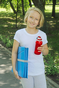 快乐女孩与一瓶水和垫为体育和瑜伽在公园里