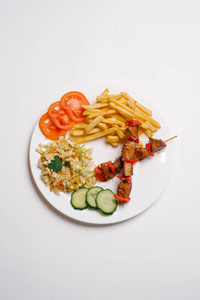法式薯条, 鸡肉串, 黄瓜切片, 西红柿, 卷心菜沙拉, 白色背景上的白盘子