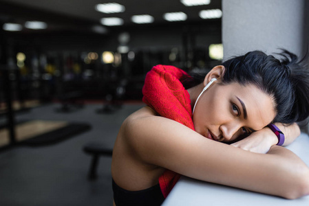 特写肖像的疲惫的年轻漂亮健身妇女俯身在健身房后, 心脏。运动员休息从她的锻炼与红色毛巾在脖子和耳机听音乐