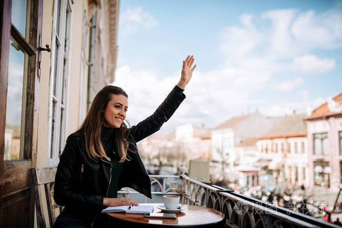 从阳台向朋友挥手的年轻女子照片-正版商用图片0o6jxf-摄图新视界