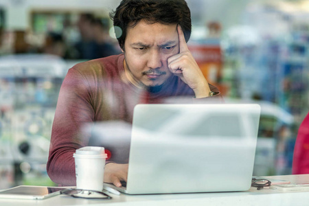 亚洲商人在休闲西装的肖像使用技术膝上型电脑在办公桌旁的桌子上, 在办公室, 商业和生活方式的概念玻璃旁边的严肃和疲惫的行动