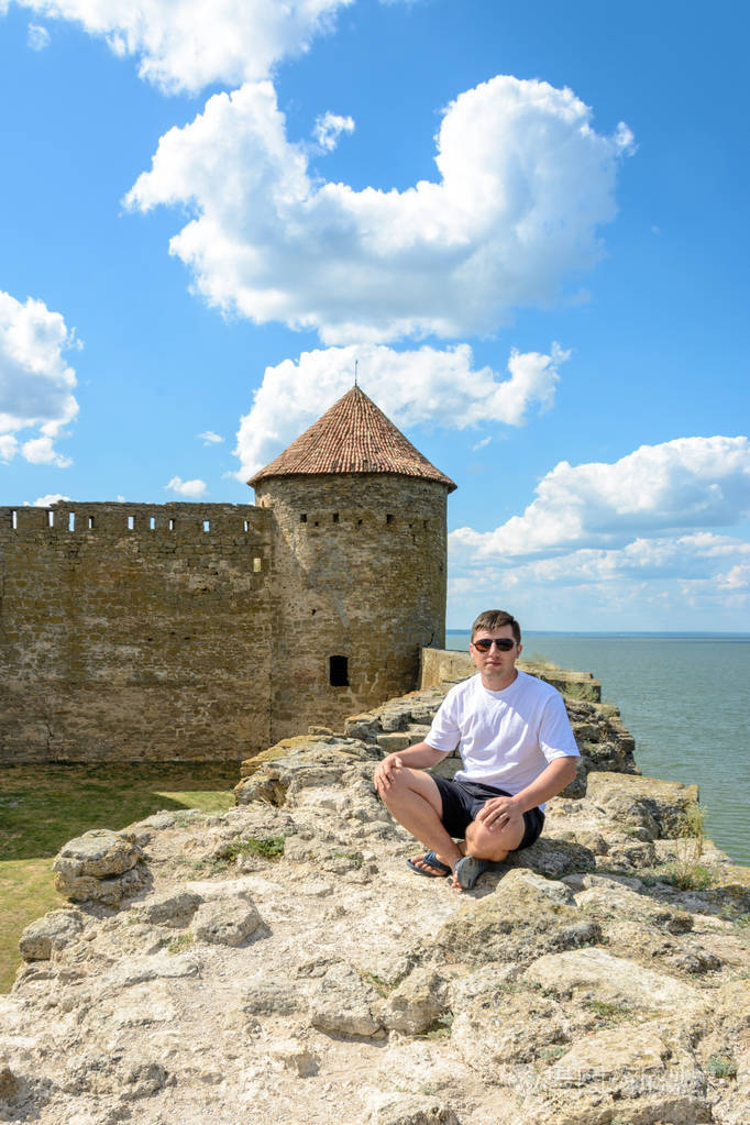 戴墨镜的年轻人坐在海边的堡垒墙上.
