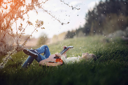 可爱的男孩躺在草地上, 吉他在日落