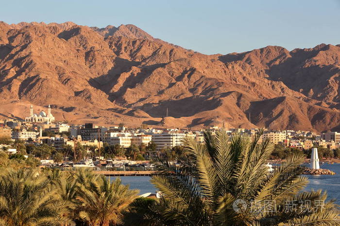 亚喀巴的一般看法在日落与棕榈树在前景和山在背景乔丹中东