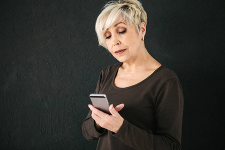 一位积极的现代老年妇女手持手机, 正在使用它。老一辈与现代科技