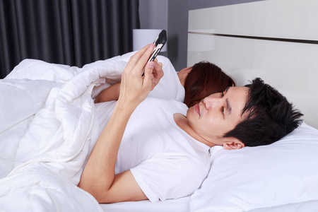 男子在床上使用手机, 而他的妻子正在睡觉。