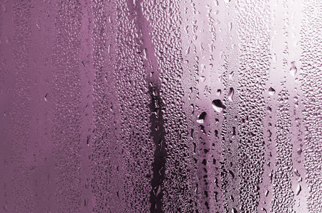 质地的一滴雨在玻璃湿透明的背景上。粉红色色调色调