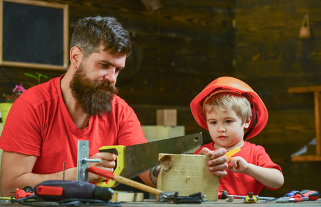男孩, 孩子忙于防护头盔学习使用手锯与爸爸。父亲, 父母用胡子教小儿子用锋利的手锯锯, 木匠工艺品。男性责任概念
