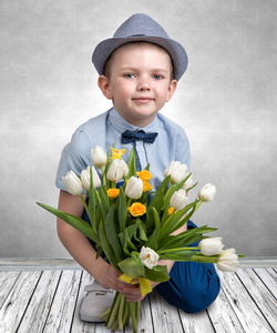 在一顶帽子，拿着一束春天郁金香的时尚男孩。儿童时装