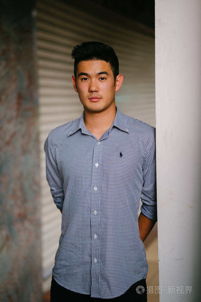 一个英俊, 年轻, 聪明的中国亚裔男子的肖像微笑着, 站在墙上的一天.