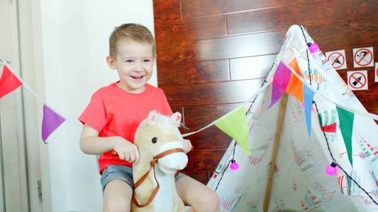 小快乐男孩骑着玩具马在游戏室里
