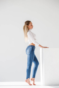 金发女郎的肖像穿着蓝色牛仔裤和白色的衬衫站在白色工作室背景