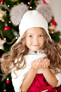 雪在她手里拿着一顶帽子的女孩。在后台的圣诞树