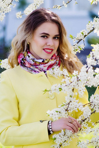 一个穿着时髦黄色大衣的年轻女子在开花的公园里。站在白色的花朵上微笑着在树枝上举行